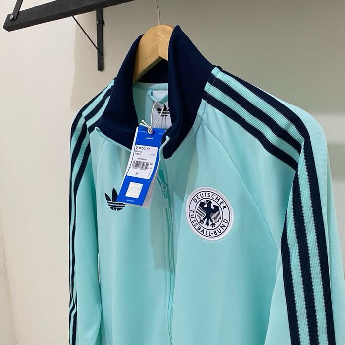 Adidas Jaket Olahraga Biru Muda dengan Logo Tim Nasional Jerman dan Tiga Garis Hitam di Sisi